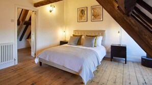 A bedroom with a wooden ceiling, a bed with a white bedspread, two wall-mounted lamps, and a radiator. - Host & Stay | The Coach House (Whitby)
