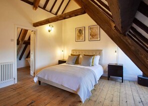 Un dormitorio con techo de madera, una cama con colcha blanca, dos lámparas de pared y un radiador.