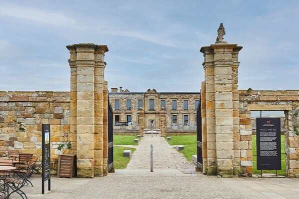 A stone building with a central entrance, a paved pathway leading to it, and a signboard on the right.
