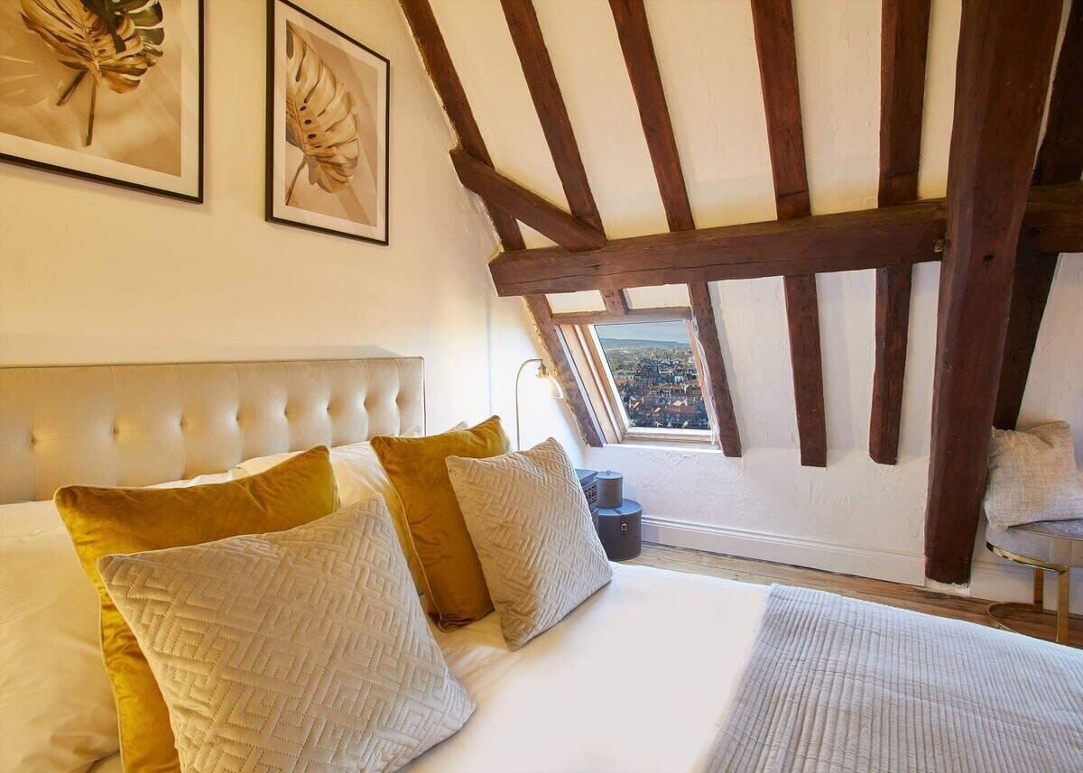 A bedroom with a bed, pillows, a headboard, a window with a view, and wooden beams.
