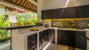 Una cocina moderna con gabinetes oscuros, protector contra salpicaduras de mármol y una isla integrada con un lavamanos y un bol de frutas.