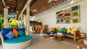 Un espacio interior amplio con techo alto, un área de comedor y un rincón de descanso con cojines de colores.