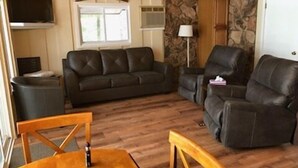 A living room with a dark leather sofa, a wooden dining table, and a stone accent wall.