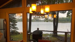 A dining area with a view of a lake and a grill outside.