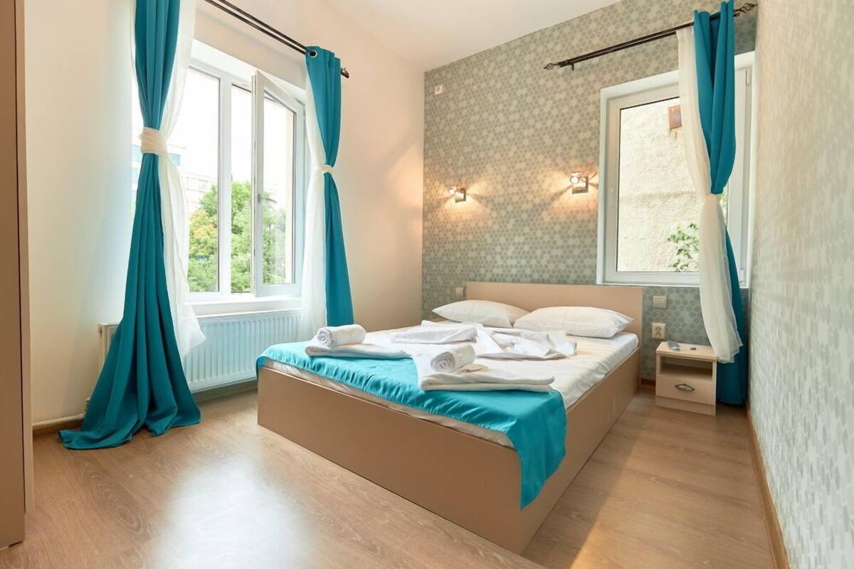 Ein Schlafzimmer mit einem Bett, einem Nachttisch, einem Fenster mit Vorhängen und einer Wandleuchte.
