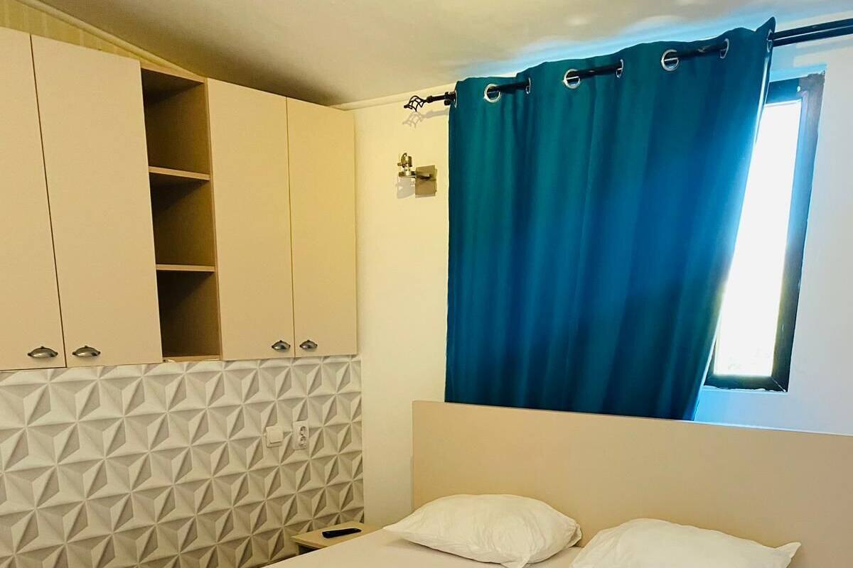 Ein Schlafzimmer mit einem Bett, weißen Kissen, einem blauen Vorhang und einem Kopfteil mit geometrischem Muster.