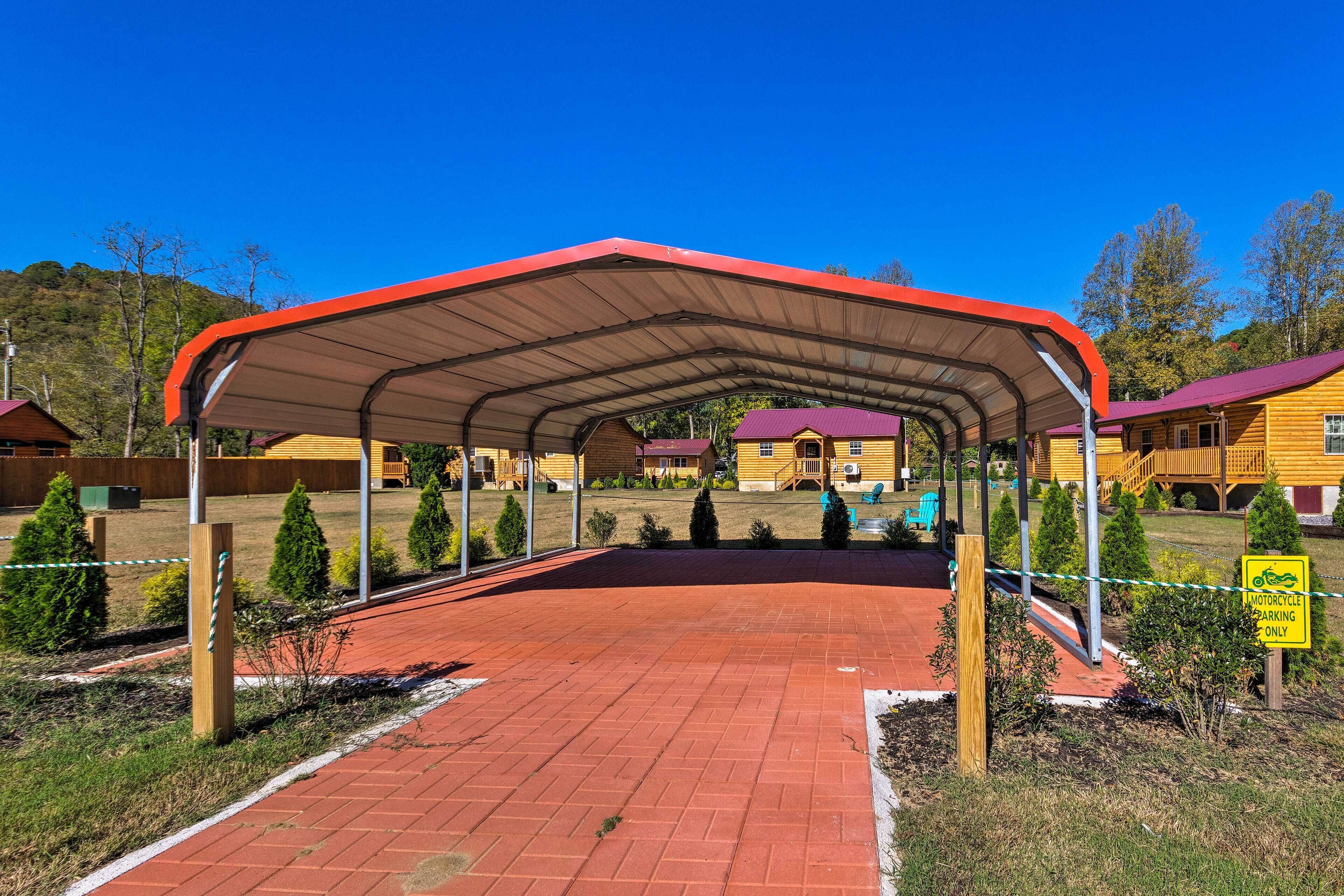 Un espacio al aire libre cubierto con techo rojo, rodeado de pequeños árboles y un edificio amarillo al fondo.