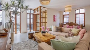 Amplia sala de estar con un sofá grande, una mesa de centro y un mueble de madera. Hay un ventanal con vistas al exterior.