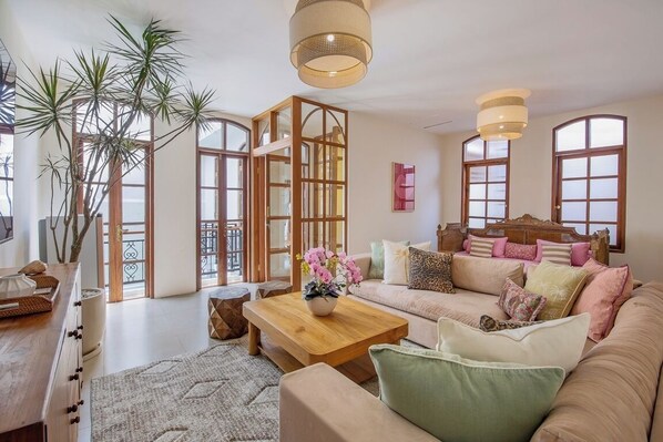 A spacious living room with a large sofa, a coffee table, and a wooden cabinet. There is a large window with a view of the outside. - Villa Casa Adeline (Kerobokan)