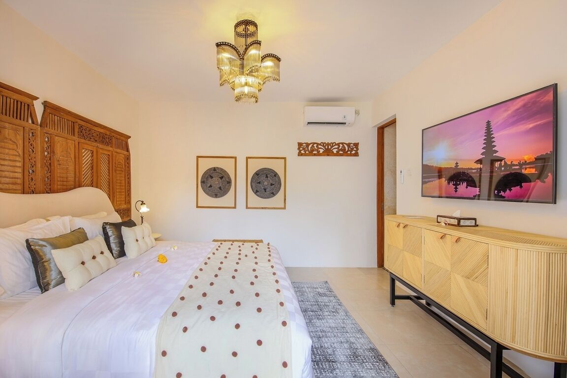 A bedroom with a bed, a TV, a chandelier, and artwork on the wall.