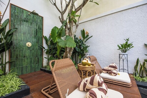 A cozy outdoor seating area with a wicker chair, cushions, and a small table with a plant. - Villa Casa Adeline (Kerobokan)