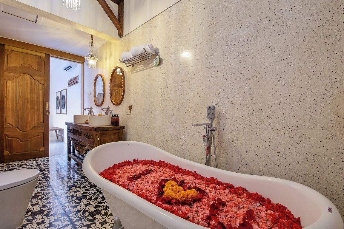 Un bagno con una vasca freestanding piena di petali di rosa, un mobile bagno in legno e uno specchio.