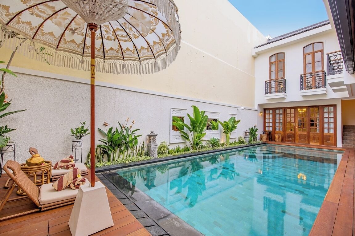A swimming pool with a wooden deck, lounge chairs, and an ornate umbrella.