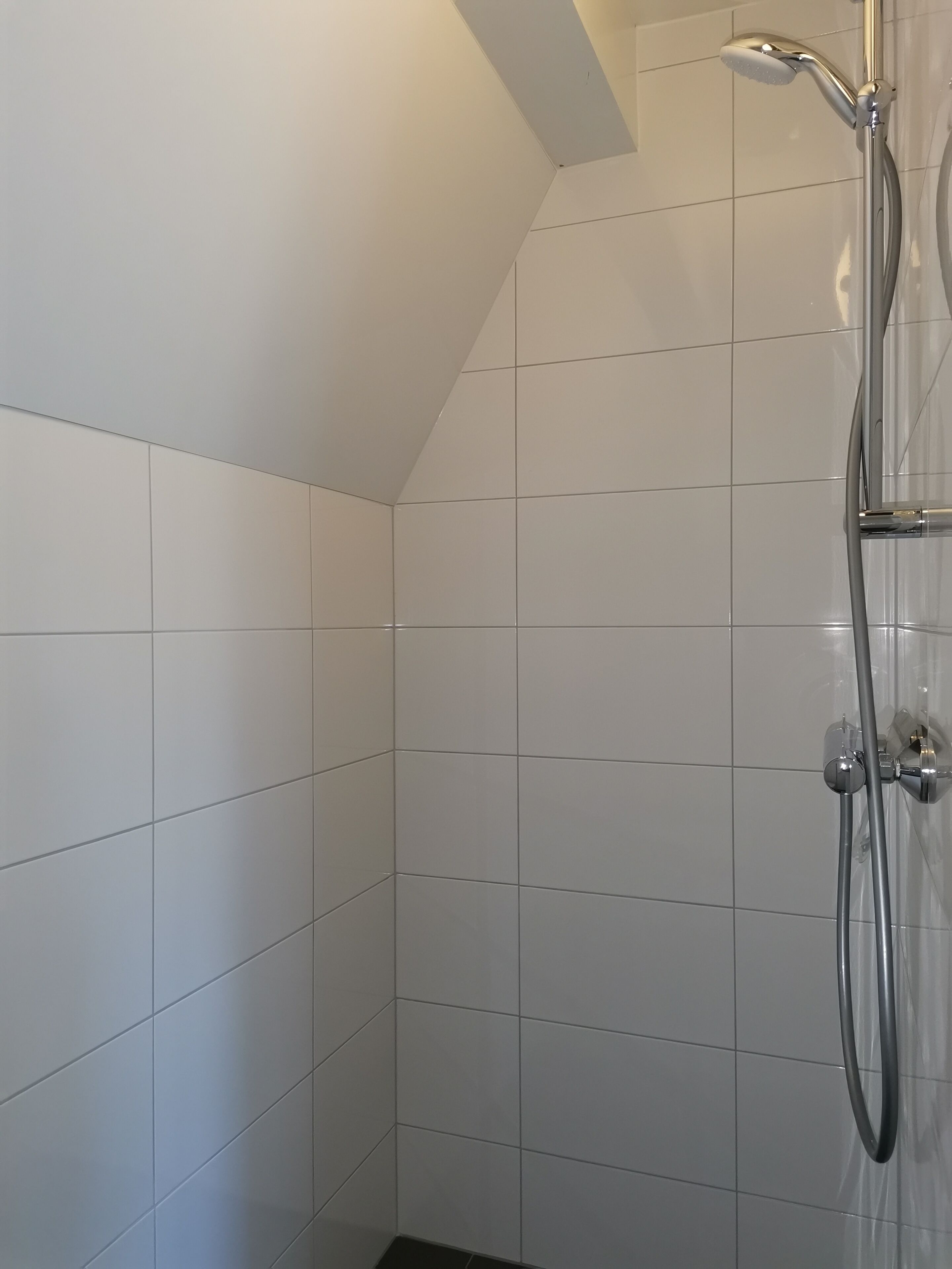 A shower with a handheld showerhead and a wall-mounted faucet in a tiled room.