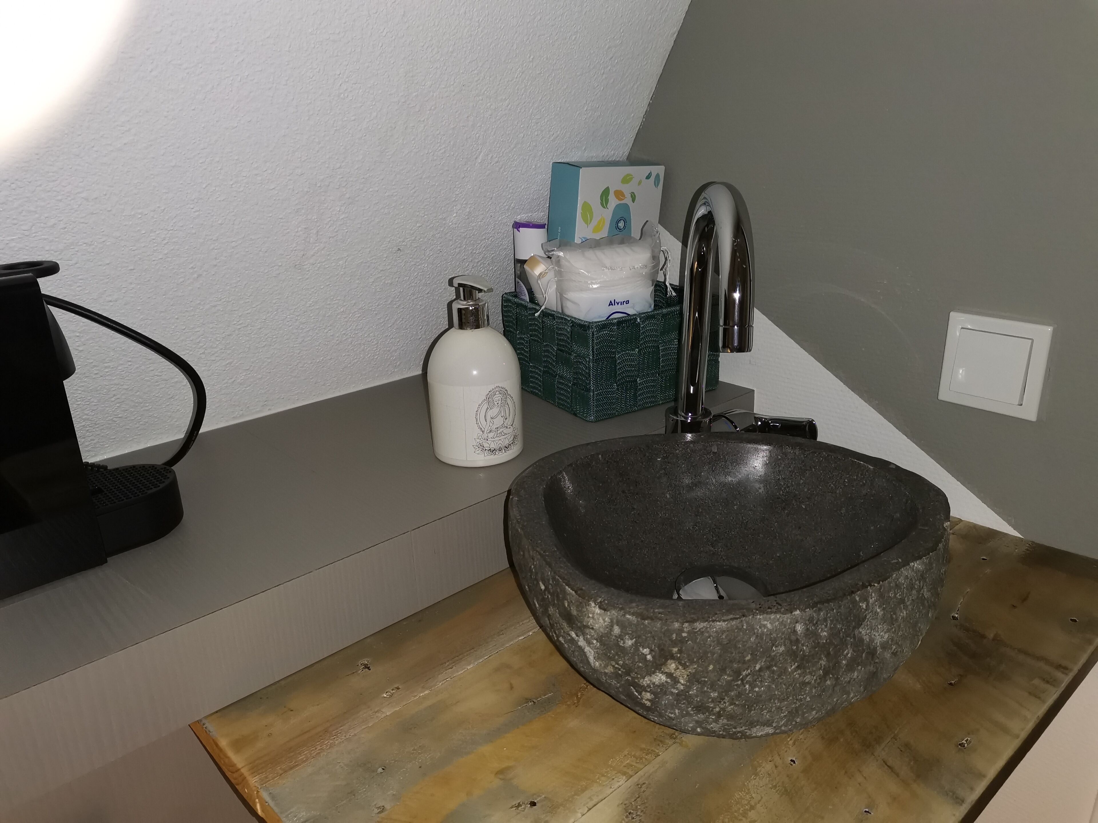A bathroom with a stone sink, a faucet, a soap dispenser, and a green basket with toiletries.