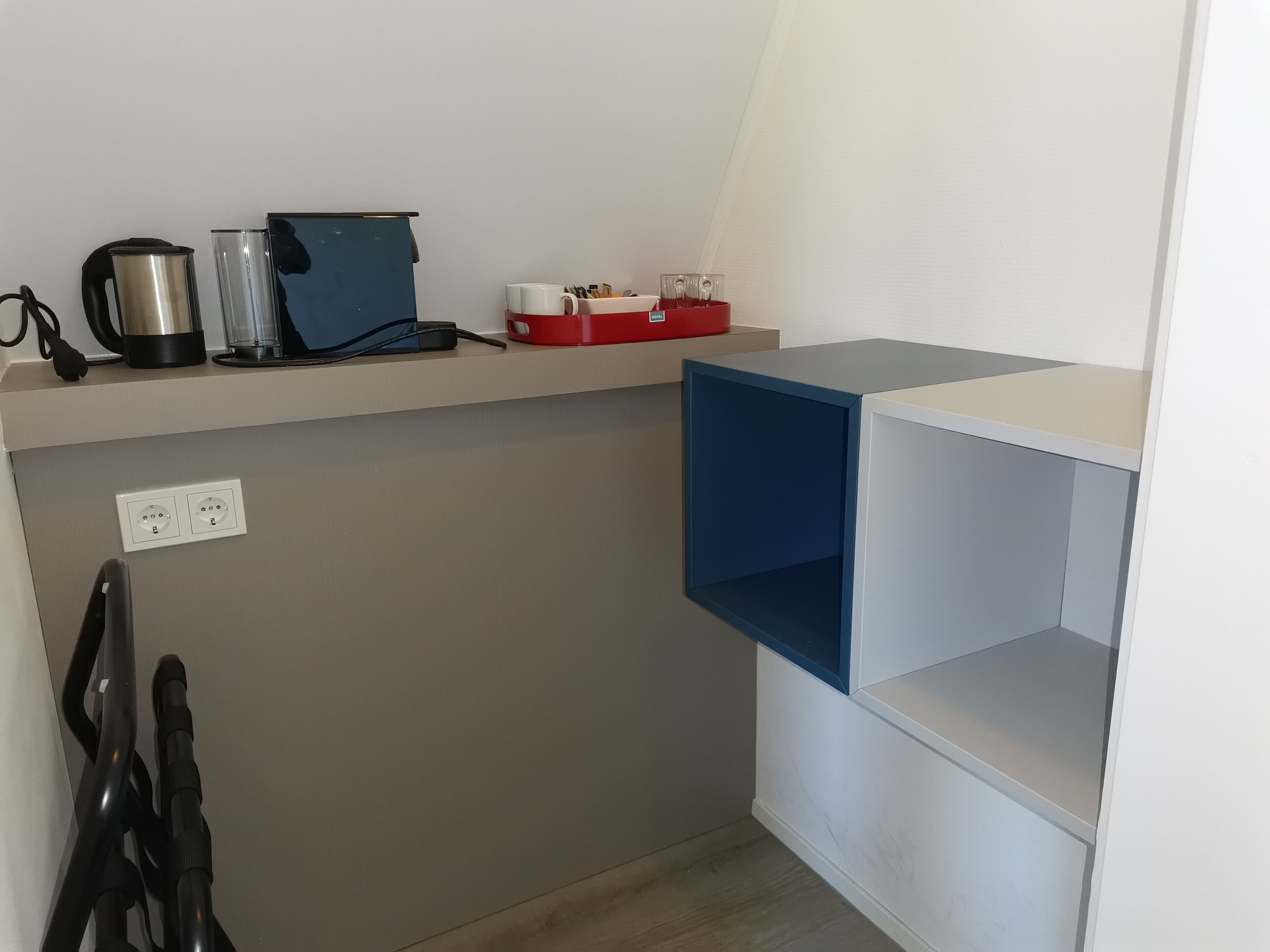 Une cuisine équipée d’un plan de travail, d’une bouilloire, d’une machine à café et d’une boîte de rangement rouge.