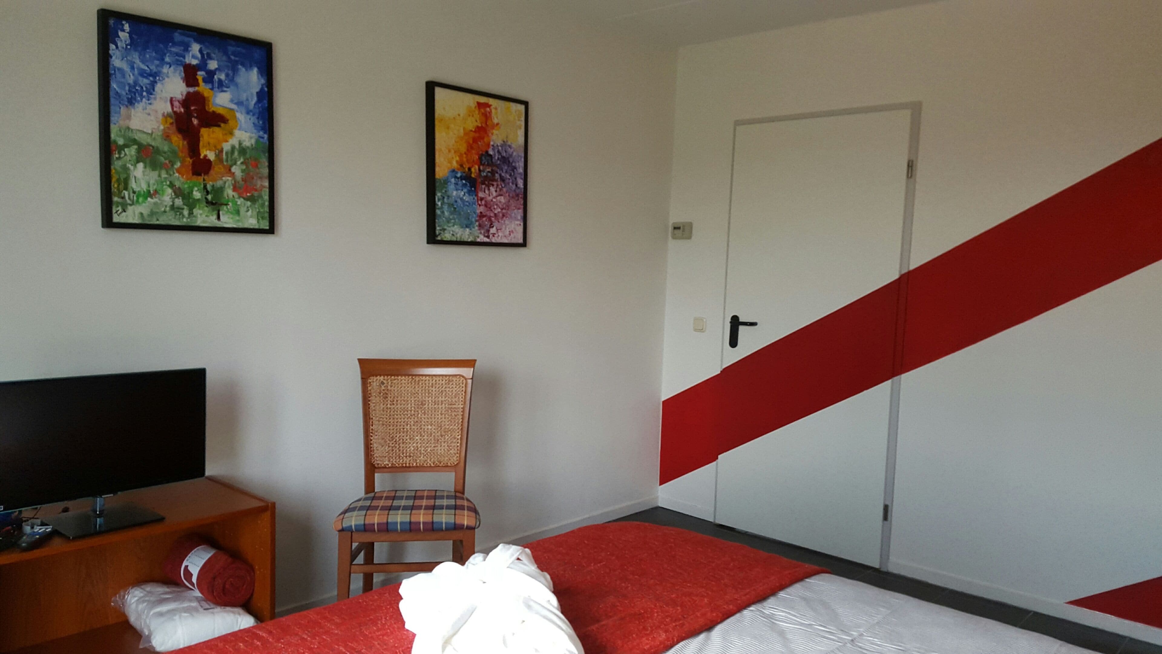 Une chambre d’hôtel avec un lit, une chaise, un téléviseur et deux tableaux accrochés au mur.