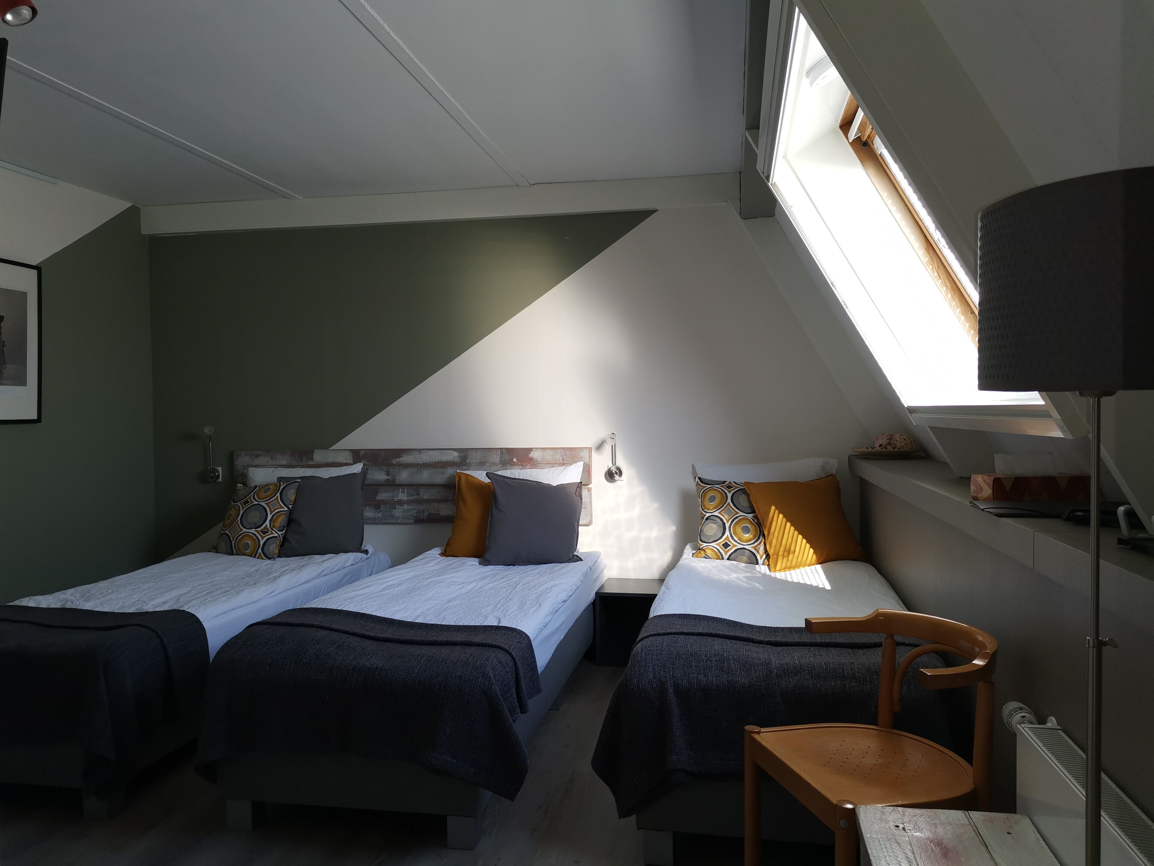 A room with two beds, a wooden chair, a radiator, and a window with a view.