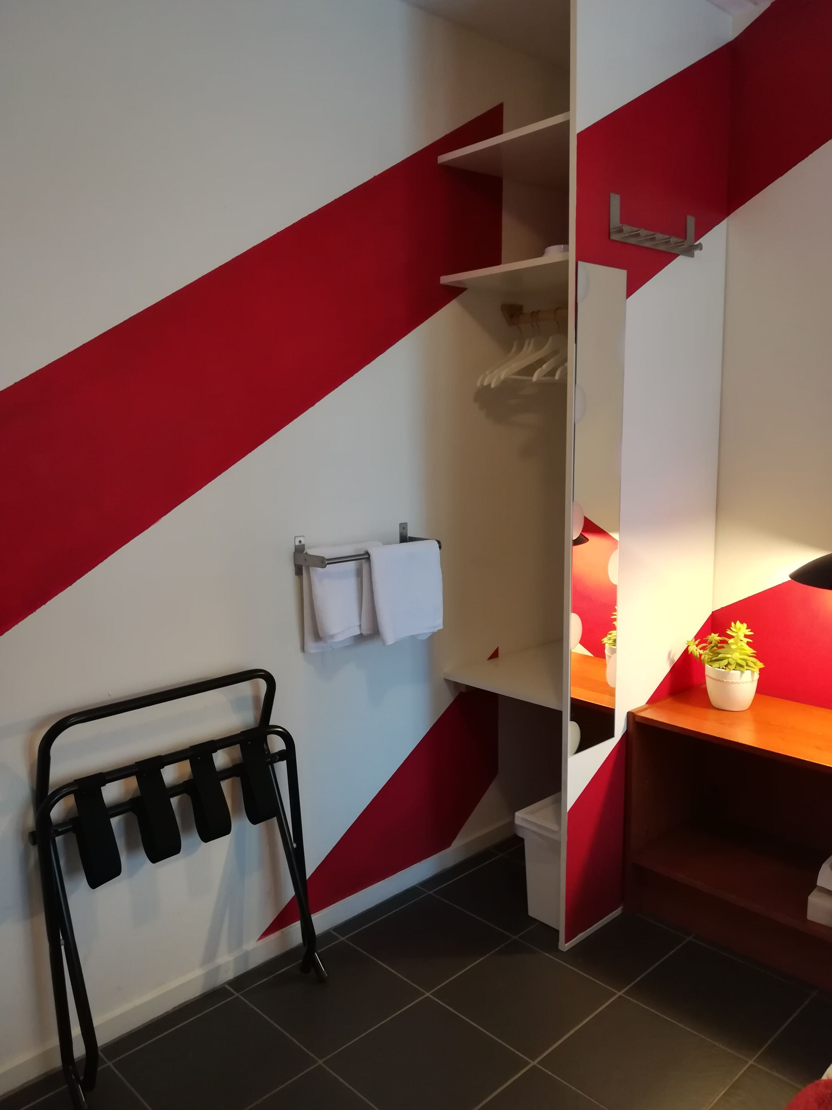 A modern bathroom with a red and white color scheme, a towel rack with white towels, a black towel rack, and a small potted plant on a wooden shelf.