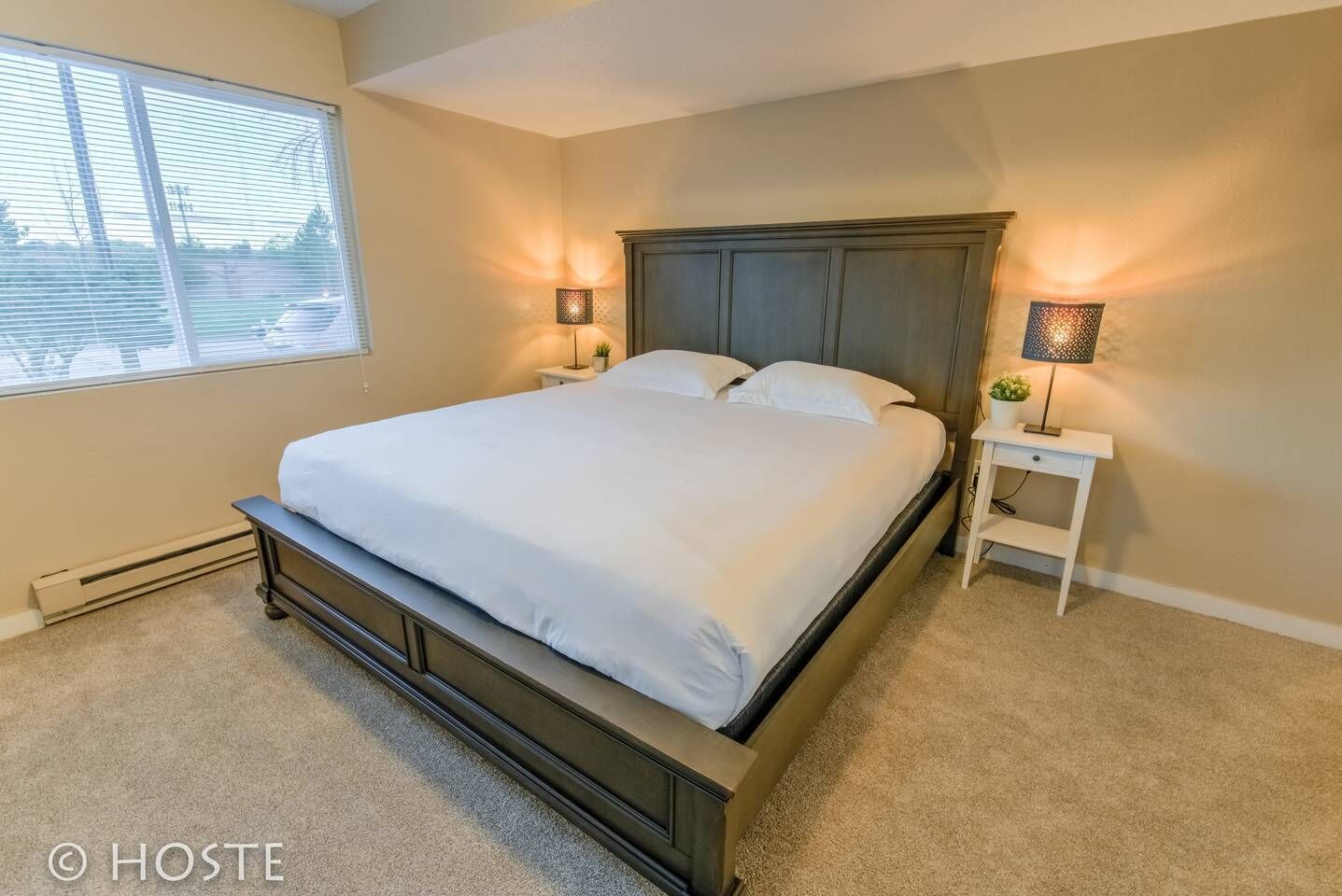 A bedroom with a large bed, two bedside tables, and a window with blinds.