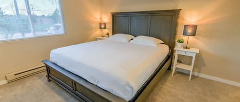 A bedroom with a large bed, two bedside tables, and a window with blinds.