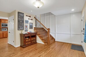 A spacious living room with hardwood flooring, a wooden staircase, and a kitchen area with wooden cabinets and a microwave.