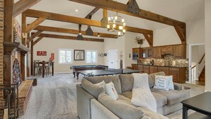 Un salón amplio con mesa de billar, un sofá con cojines decorativos y una zona de cocina con armarios de madera.