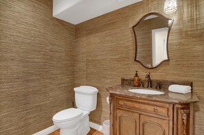 A bathroom with a wooden wall, a white toilet, a sink with a marble countertop, and a wooden vanity.