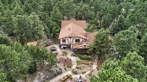Una casa grande rodeada de árboles frondosos, con un patio y una pequeña terraza.