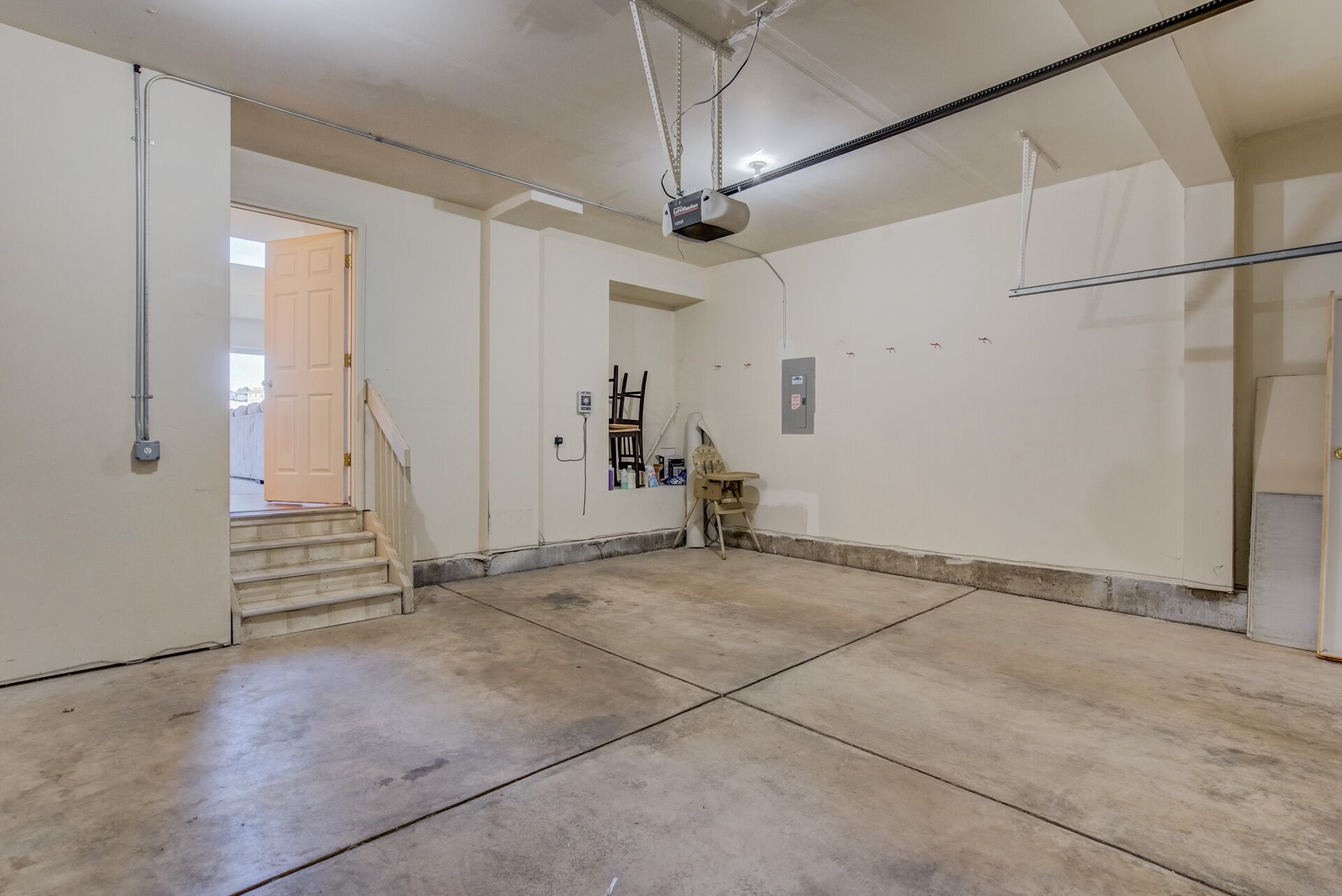 A spacious garage with concrete floors and white walls, a ceiling fan, and a wooden chair.
