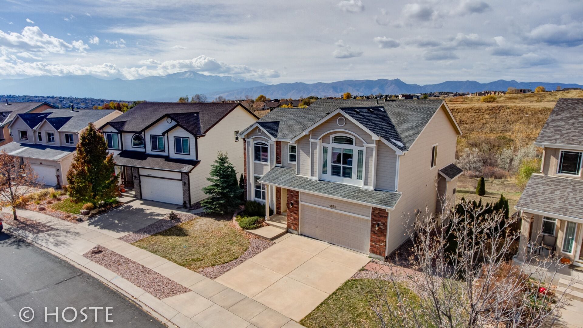 A residential area with houses featuring gabled roofs and brick accents, set against a backdrop of mountains.