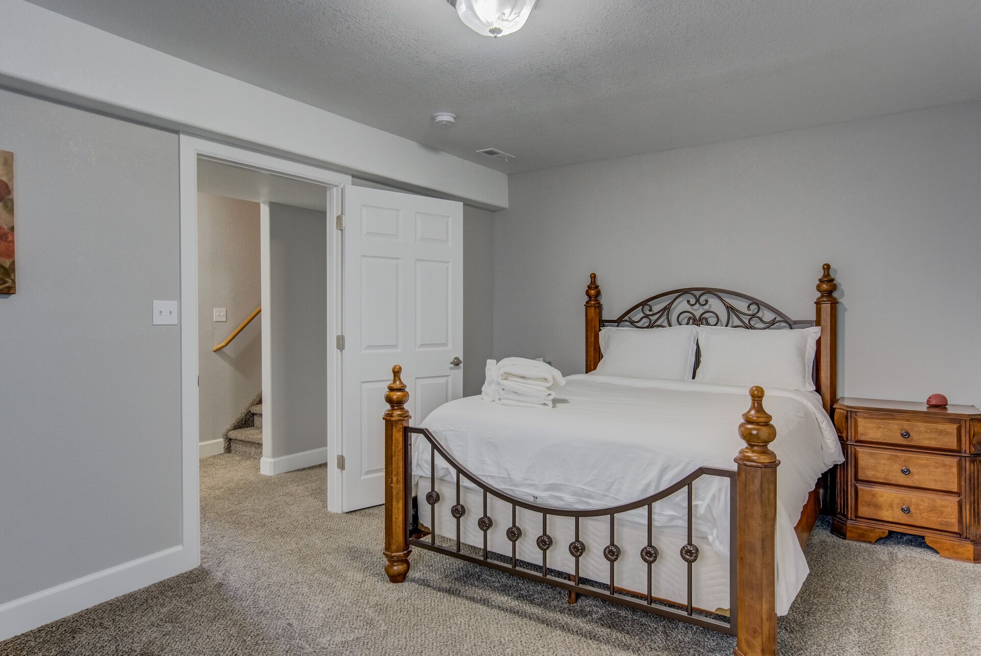 Een slaapkamer met een bed, een houten dressoir en een deur naar een andere kamer.