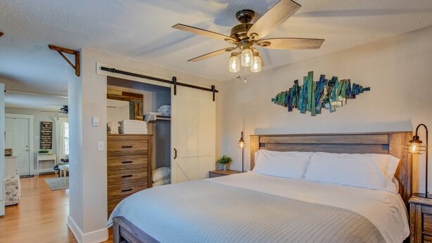 A bedroom with a large bed, wooden headboard, a ceiling fan, and a wall art piece. - Craft Brewery Perfection! Charming & Dog-friendly (Colorado Springs)