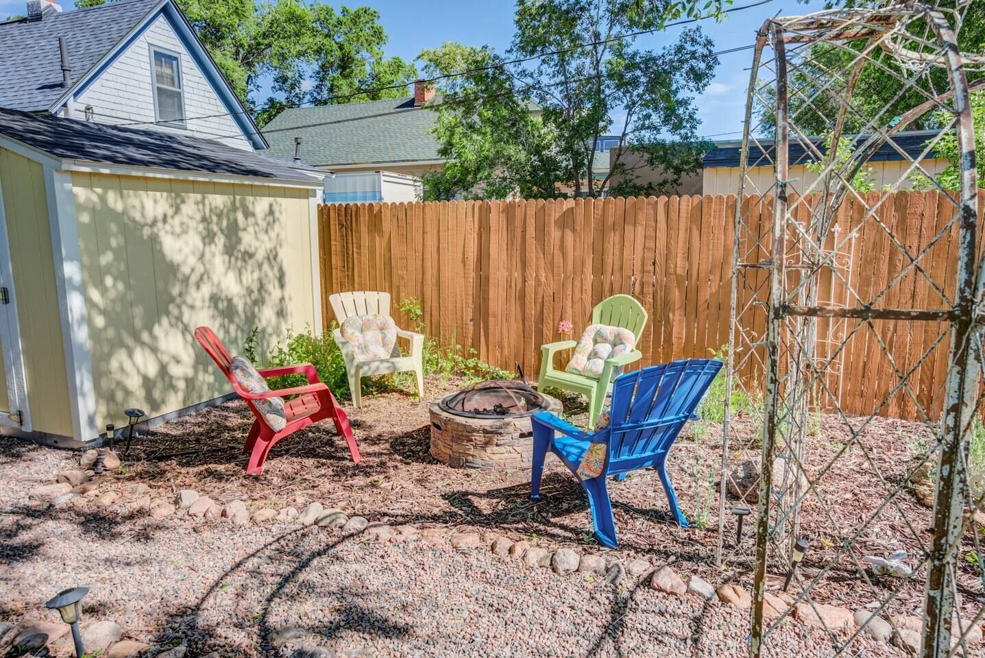 A backyard with a wooden fence, a shed, and three Adirondack chairs.