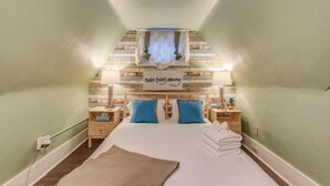 Um quarto aconchegante com teto inclinado, uma cama com almofadas azuis, uma placa com a frase 'faça hoje incrível' e um pequeno cacto na mesa de cabeceira.