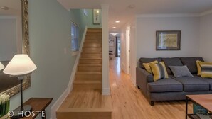 A living room with a grey sofa, wooden staircase, and a framed picture on the wall.
