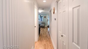 A hallway with white doors, a wooden floor, and a dining area in the background.