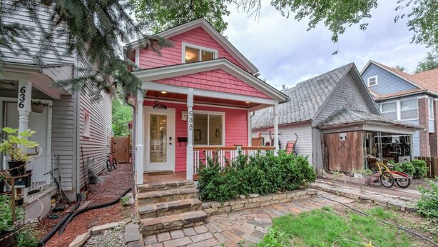 A two-story house with a red front, a porch, and a small garden area.