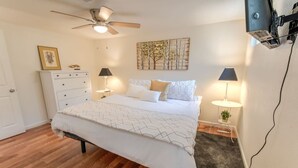 A bedroom with a bed, two bedside tables with lamps, a ceiling fan, a dresser, and a painting on the wall.