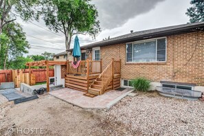 A backyard with a wooden deck, a covered patio, and a brick house.