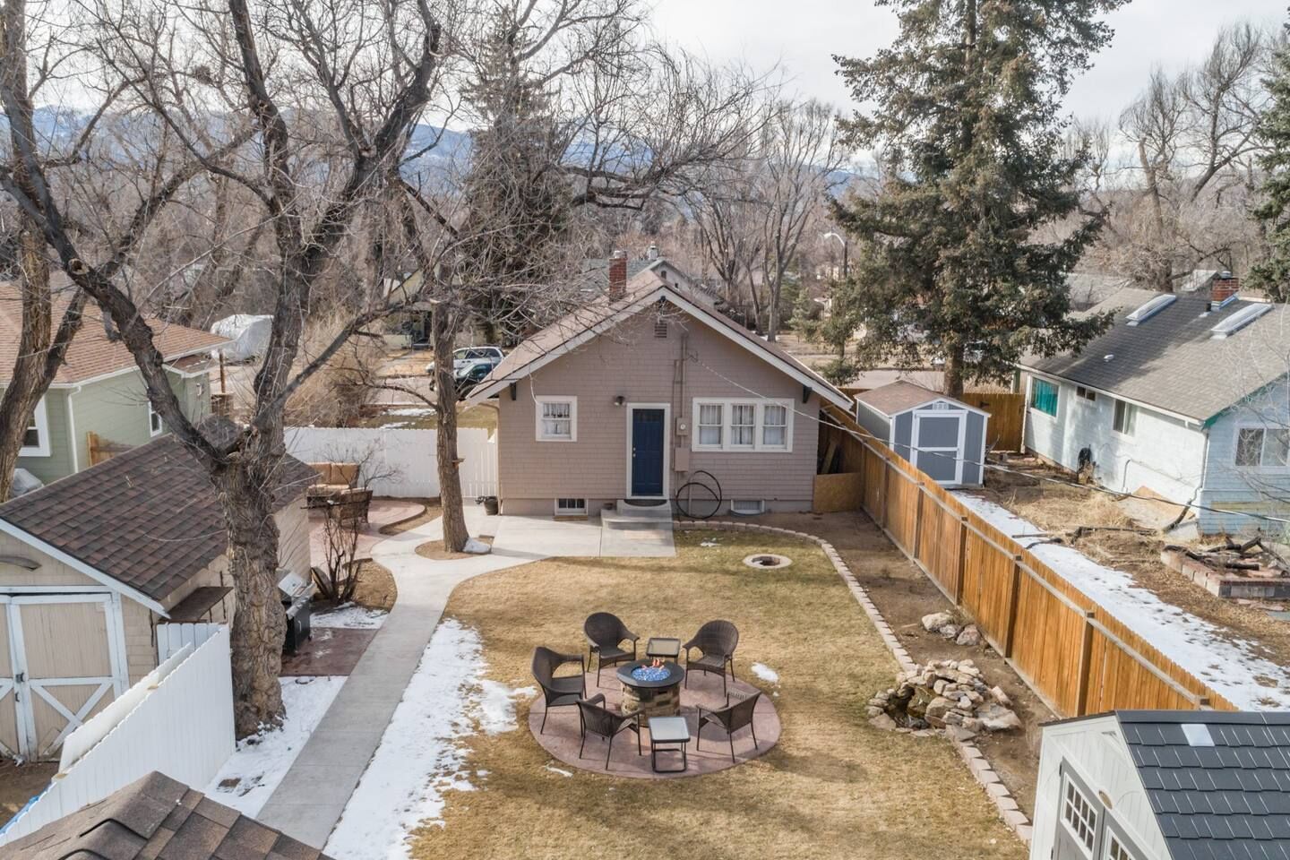 A residential backyard with a circular patio, a small house, and a wooden fence.
