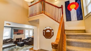 Un escalier avec des rampes en bois menant à l’étage supérieur, un salon doté d’une cheminée et un grand drapeau américain.
