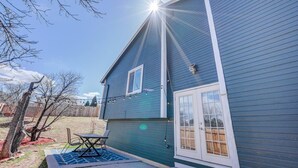 A two-story house with a blue exterior, a covered patio with a table and chairs, and a visible garage door. - 4BR Garden of the Gods Family Getaway (Colorado Springs)