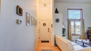 A hallway leading to a living room with a white sofa, a small table, and a window with curtains. - 4BR Garden of the Gods Family Getaway (Colorado Springs)