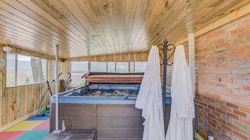 A hot tub area with a wooden ceiling, a brick wall, and a view of the outdoors.