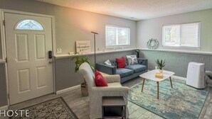 A cozy living room with a gray sofa, a striped armchair, a small white table, and a decorative wreath on the wall. - 2BR Garden-level Great Outdoors Dog Friendly (Colorado Springs)