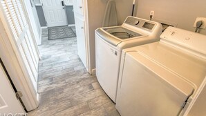 A laundry room with two front-loading washing machines, a drying rack, and a door leading to a hallway with a door and a rug. - 2BR Garden-level Great Outdoors Dog Friendly (Colorado Springs)
