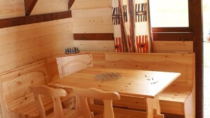 A wooden cabin interior with a wooden table and benches, a window with curtains, and a small shelf with items. - Moulin de Lachaud (Sainte-Fortunade)