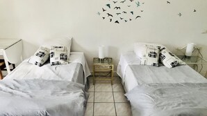 A twin room with two beds, each with grey bedding and patterned pillows. There is a wall decal of birds, a bedside table with a lamp, and a small wooden cabinet. - Moulin de Lachaud (Sainte-Fortunade)