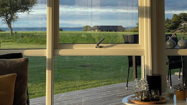 A room with large windows offering a view of a grassy field and a distant building. - Beautiful holiday home on Nordals, Vinkelbæk 40 (Nordborg)